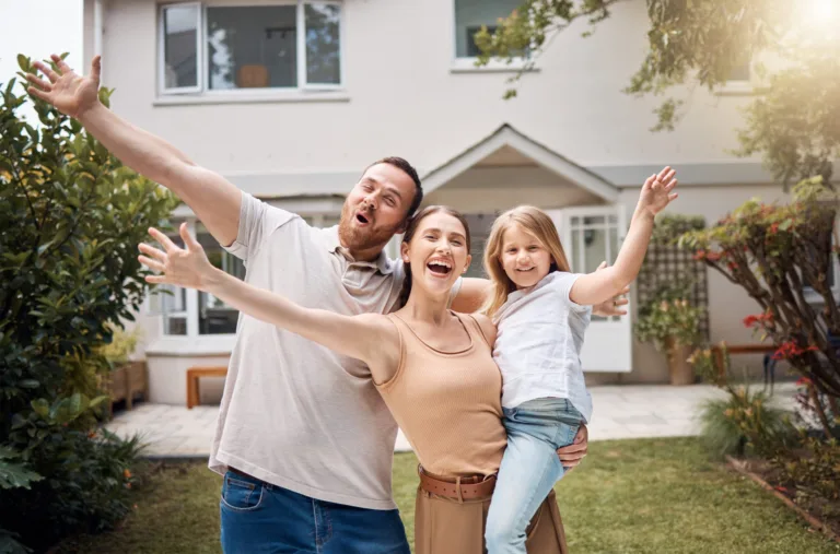 Família sorridente comemorando em frente à nova casa, representando conquista e felicidade